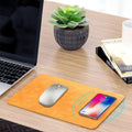 Brown leather desk mat with integrated wireless charging pad for mobile phones on a wooden desk.