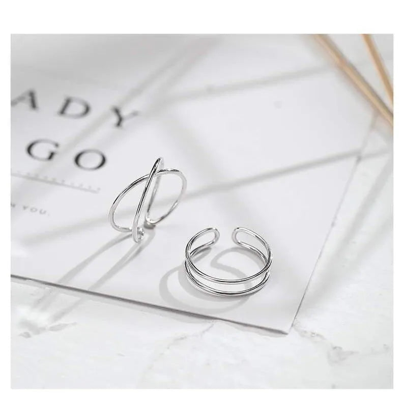 Silver plated geometric cross ring with adjustable opening on a plain background.