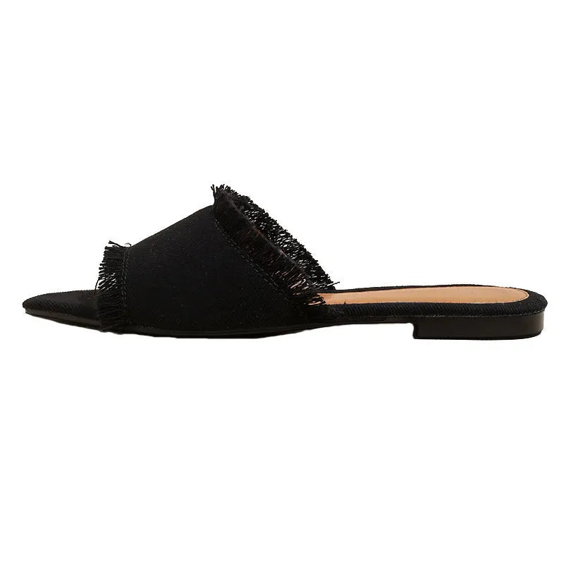 Women's solid colour denim flat slippers with a tassel detail on the front.