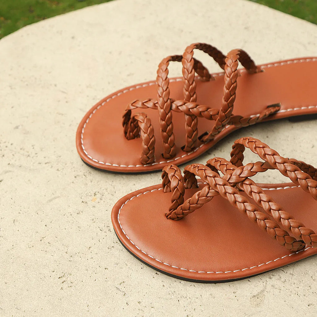 Women's brown woven clip-toe flat sandals on a light background, showing the strap detail and rubber sole.