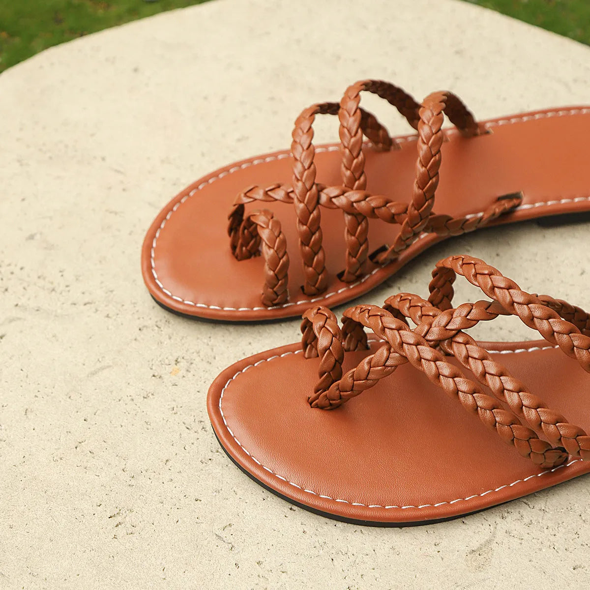 Women's brown woven clip-toe flat sandals on a light background, showing the strap detail and rubber sole.