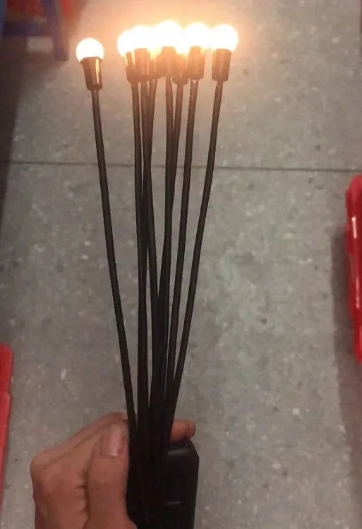 Solar-powered LED garden spike light with multiple glowing heads and a metal ground plug inserted in soil at dusk.