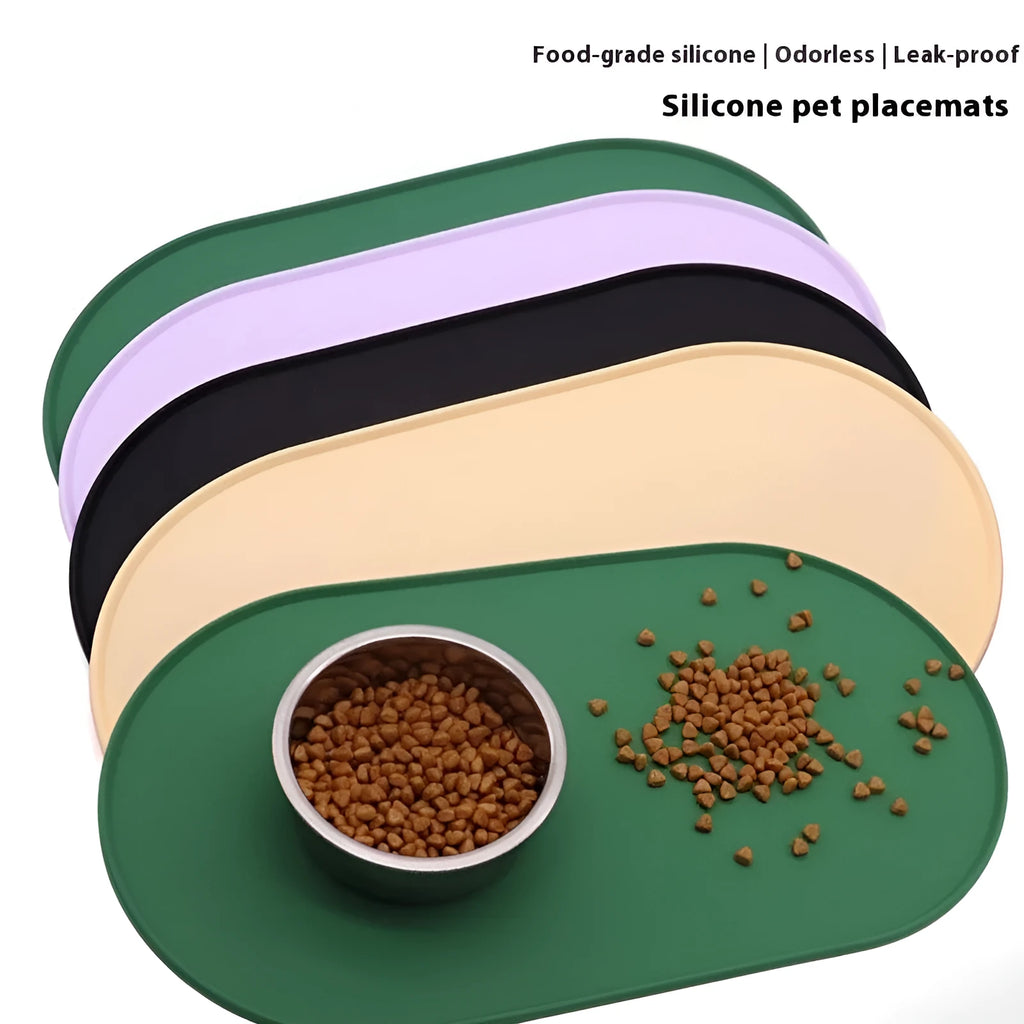 Green silicone cat feeding mat with raised edge under a ceramic food and water bowl on a wooden floor.