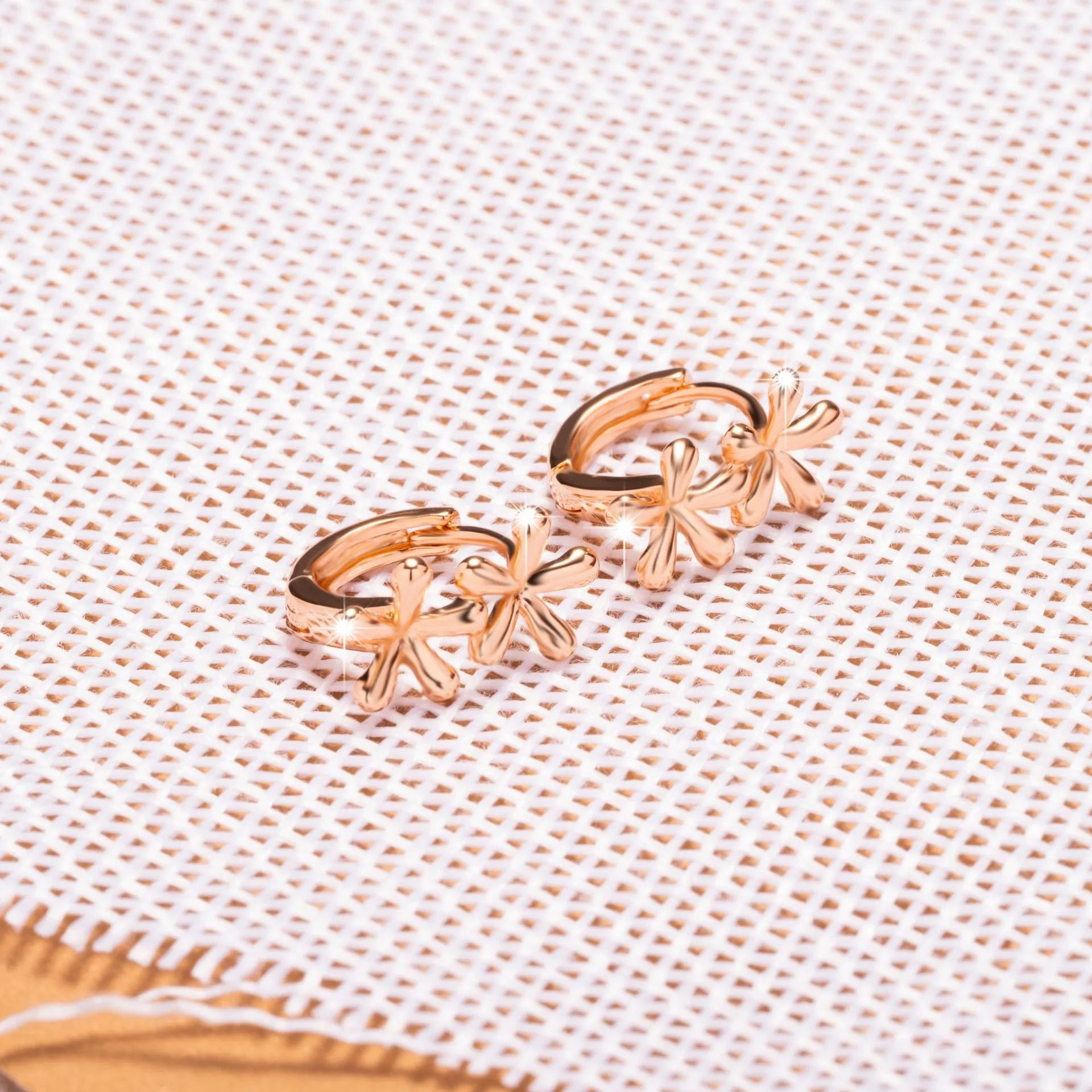 Close-up of rose gold drop earrings with 3D floral and waterdrop design on a white background.