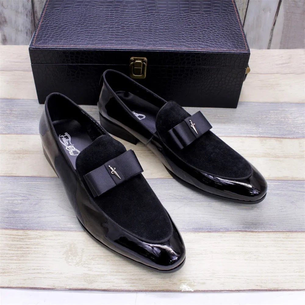 Men's black tassel loafers with glossy patent leather upper and matte leather toe holder on a wooden floor.