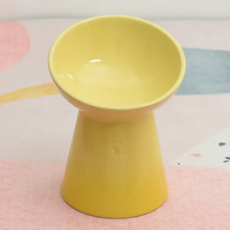 White ceramic pet bowl with black inner rim and a high, wide foot base on a wooden floor.