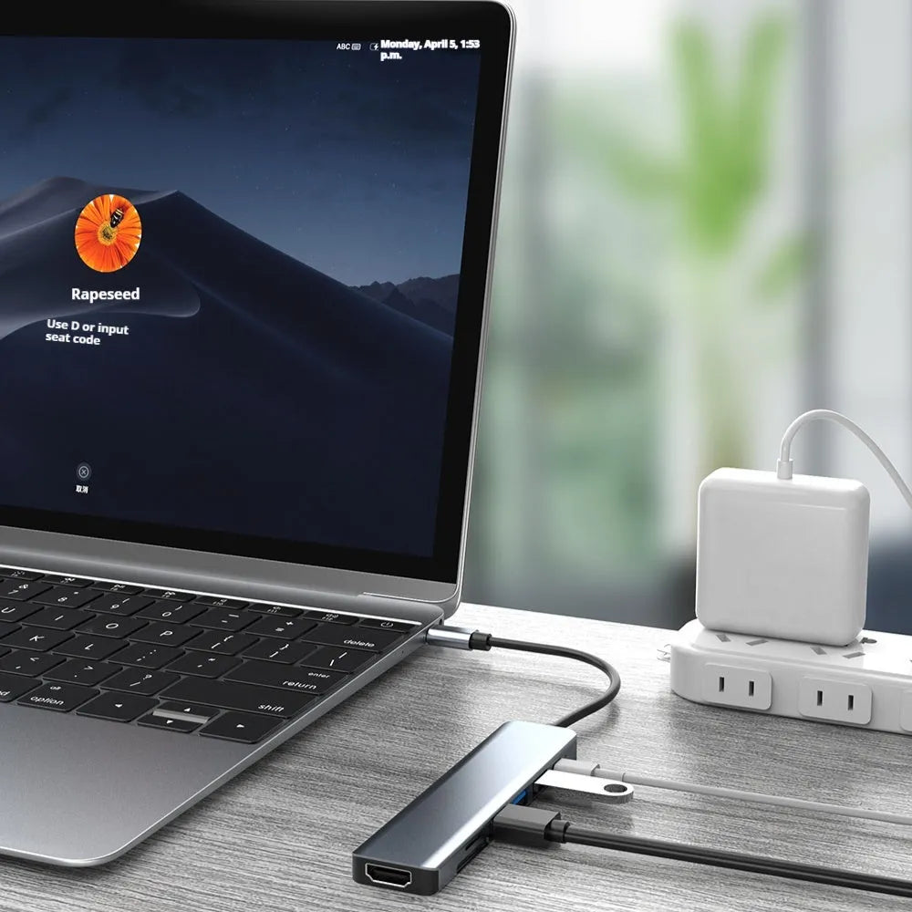 Silver seven-port type-C USB expander hub with a short black cable on a wooden desk.