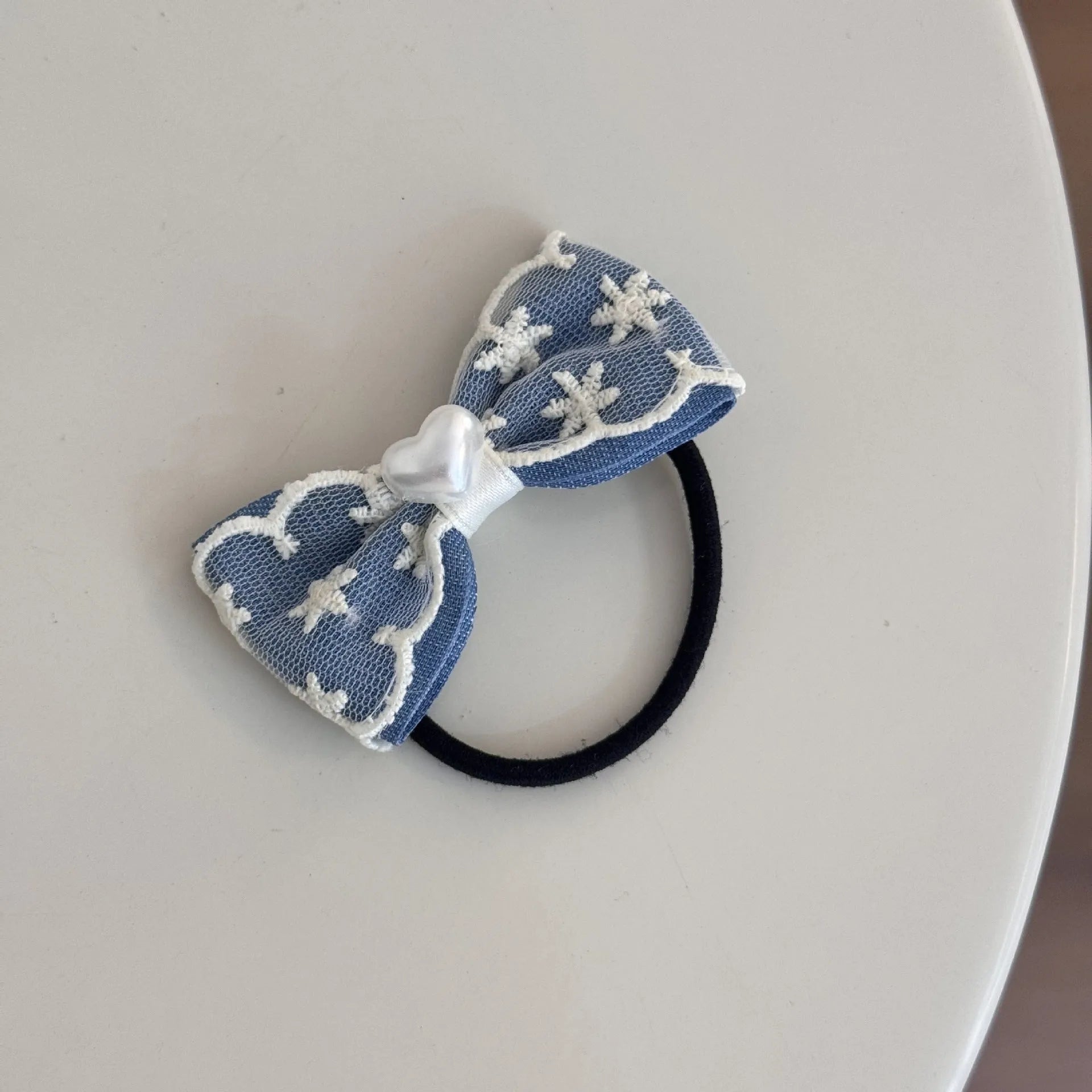 A women's hair clip barrette with a soft blue cloth bow and lace decoration on a plastic clip.