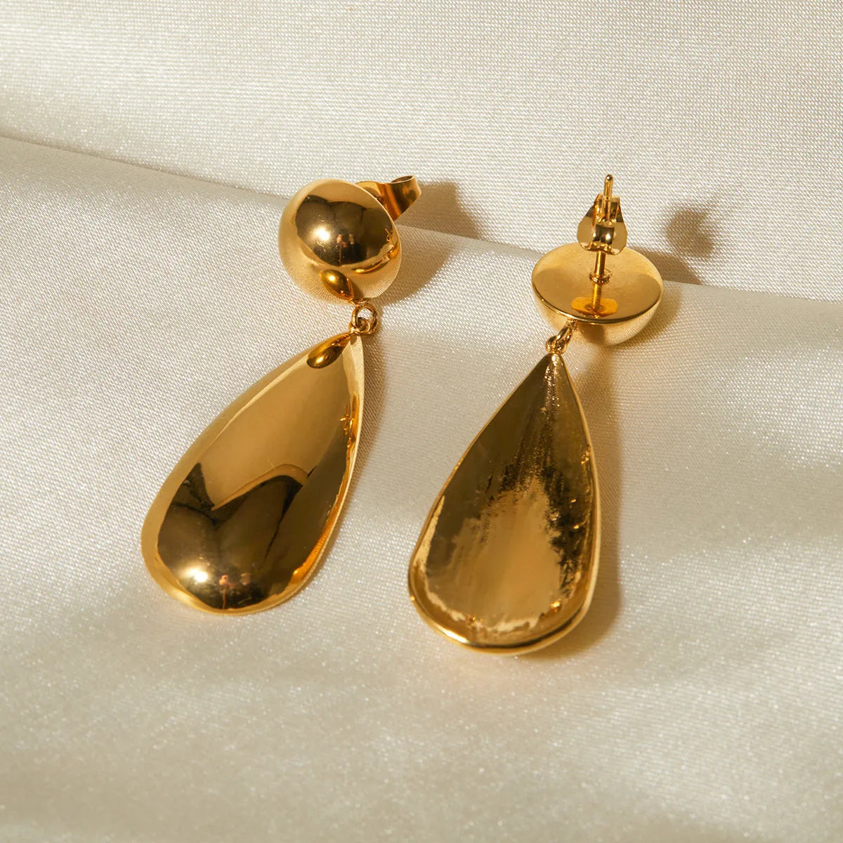 A pair of gold-coloured stainless steel pendant earrings with a geometric water drop hemisphere shape.