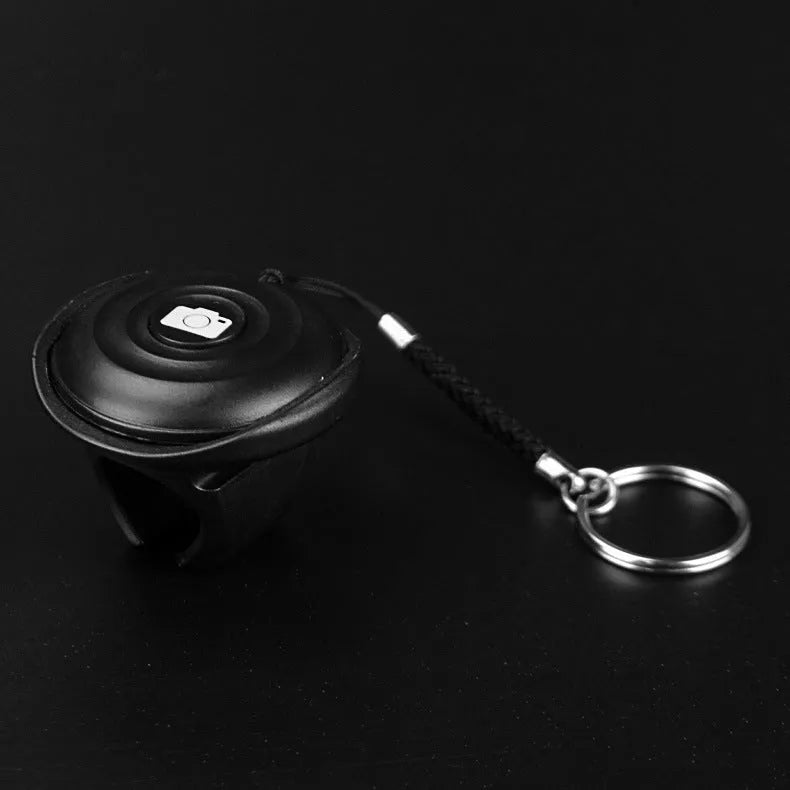 Small black Snap Bluetooth remote control for wireless smartphone camera photos on a white background.