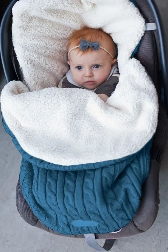 Envelope-style baby stroller sleeping bag in beige colour with thick filling, shown next to a pram.