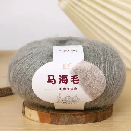 A ball of mohair yarn in a selected colour next to a hand-woven scarf example, showcasing the DIY kit.