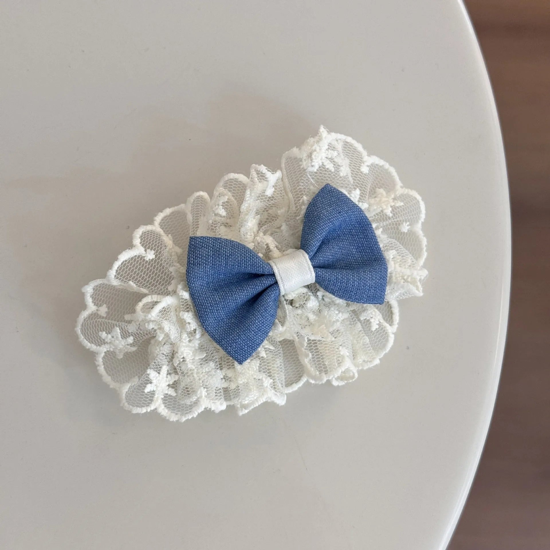 A women's hair clip barrette with a soft blue cloth bow and lace decoration on a plastic clip.