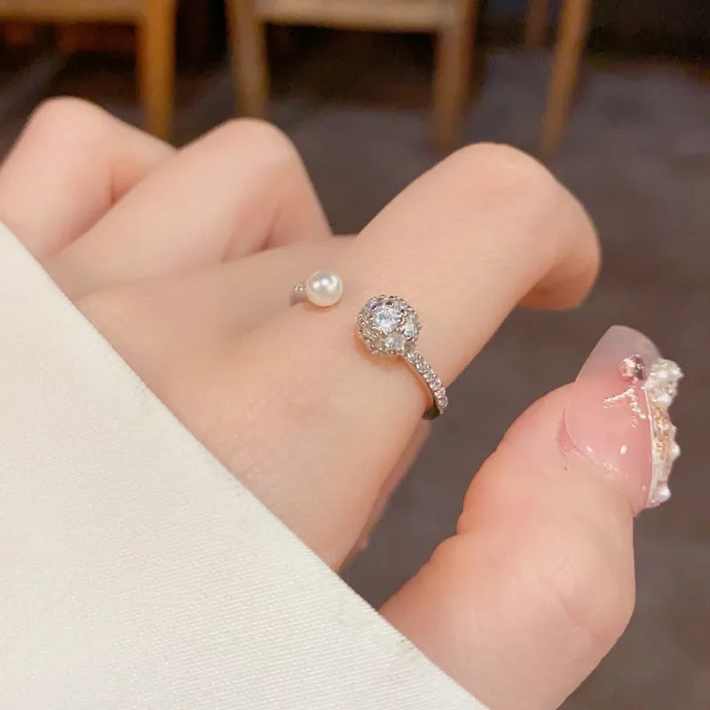 Gold or silver coloured open-end women's ring with round zircon stones and pearl detailing on a geometric band.
