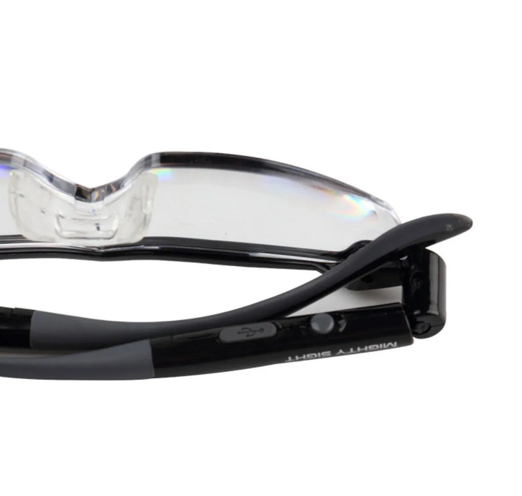 Transparent black USB rechargeable reading glasses with integrated LED light on a dark surface