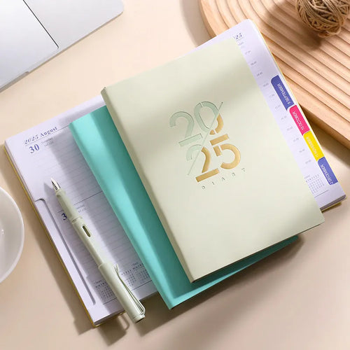 A5 2025 daily planner notebook with soft faux leather cover in multiple colours, open to show lined pages.