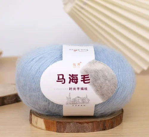 A ball of mohair yarn in a selected colour next to a hand-woven scarf example, showcasing the DIY kit.