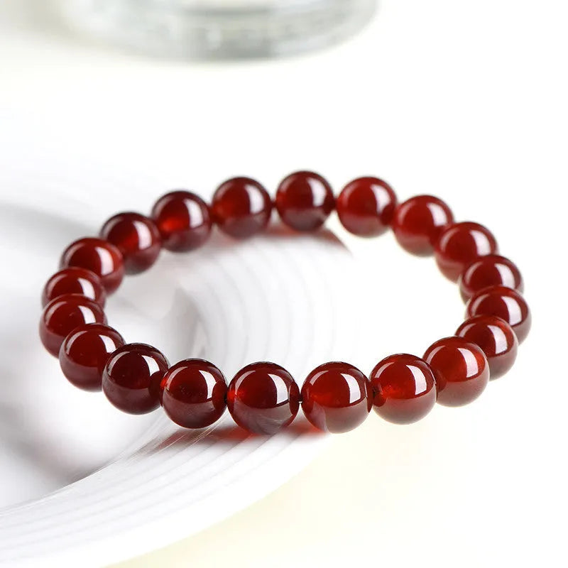 Unisex orange red garnet ball bracelet with crystal beads and a metal Ruyi charm on a wrist.