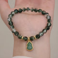 Women's citrine bracelet with green phantom quartz heart charm and pearl accents on a wrist.