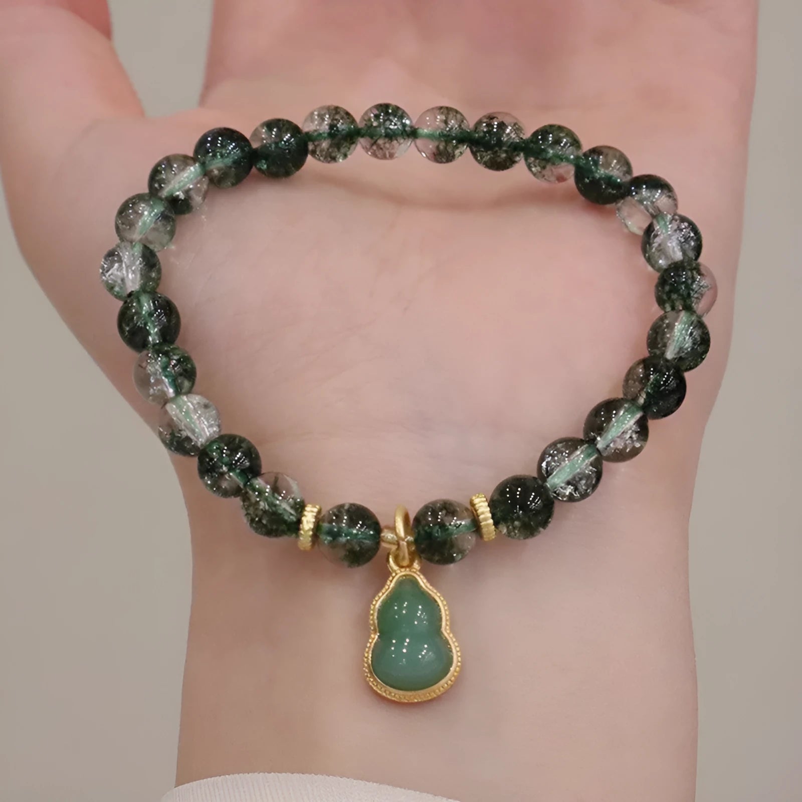 Women's citrine bracelet with green phantom quartz heart charm and pearl accents on a wrist.