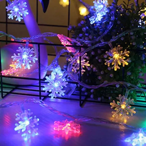 Battery powered LED snowflake string lights in warm white on a garden tree branch for Christmas decoration