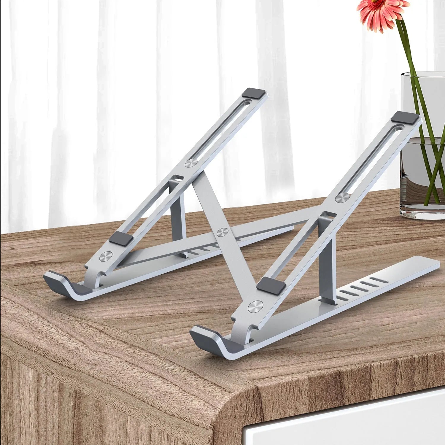Silver aluminium laptop stand folded flat next to an open laptop, showing its six-angle adjustment hinge.