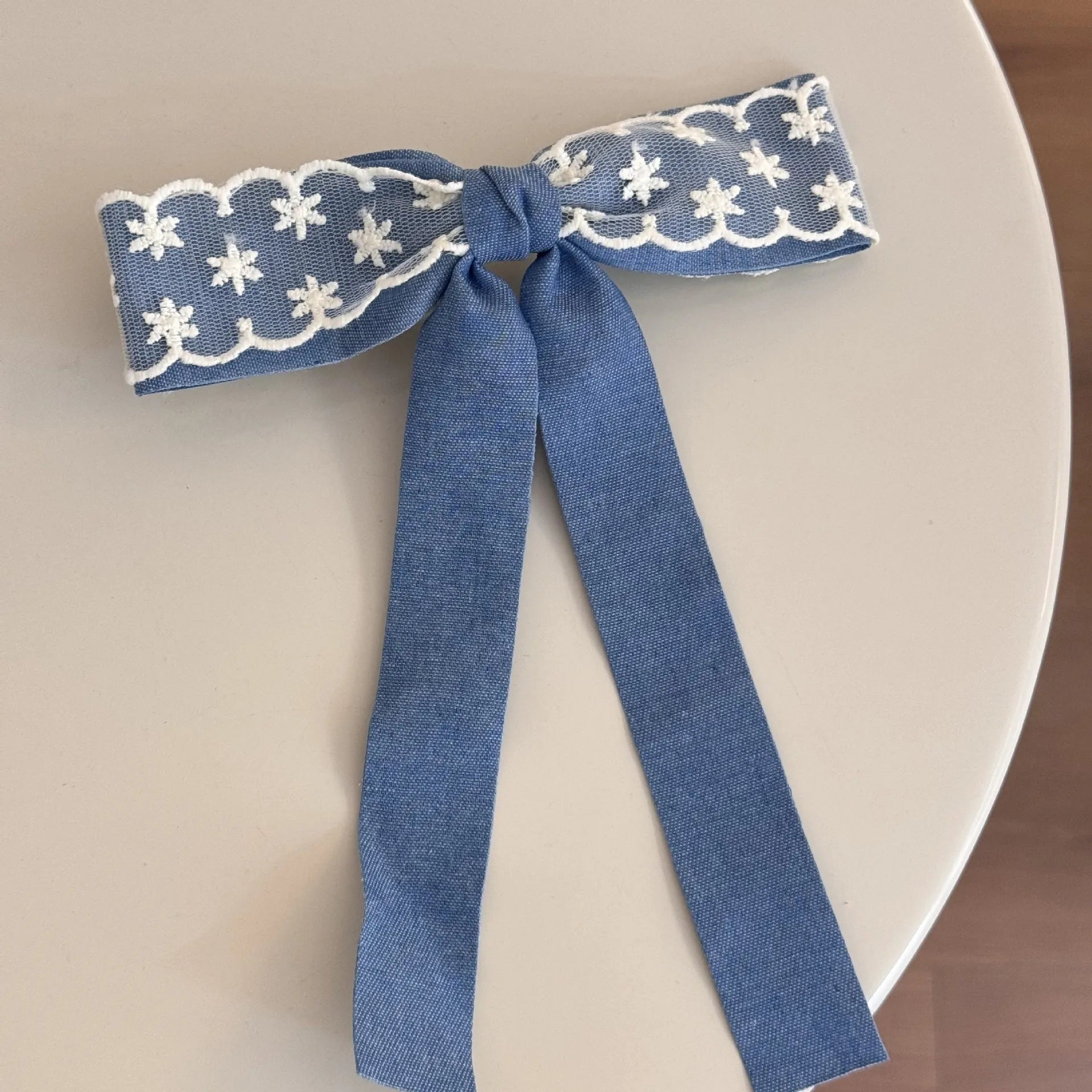 A women's hair clip barrette with a soft blue cloth bow and lace decoration on a plastic clip.