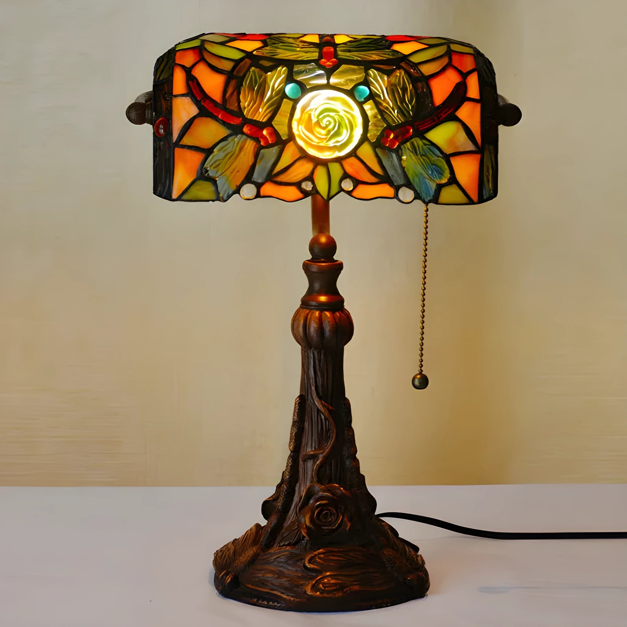 Tiffany style table lamp with coloured stained glass shade on a resin base, shown on a desk.