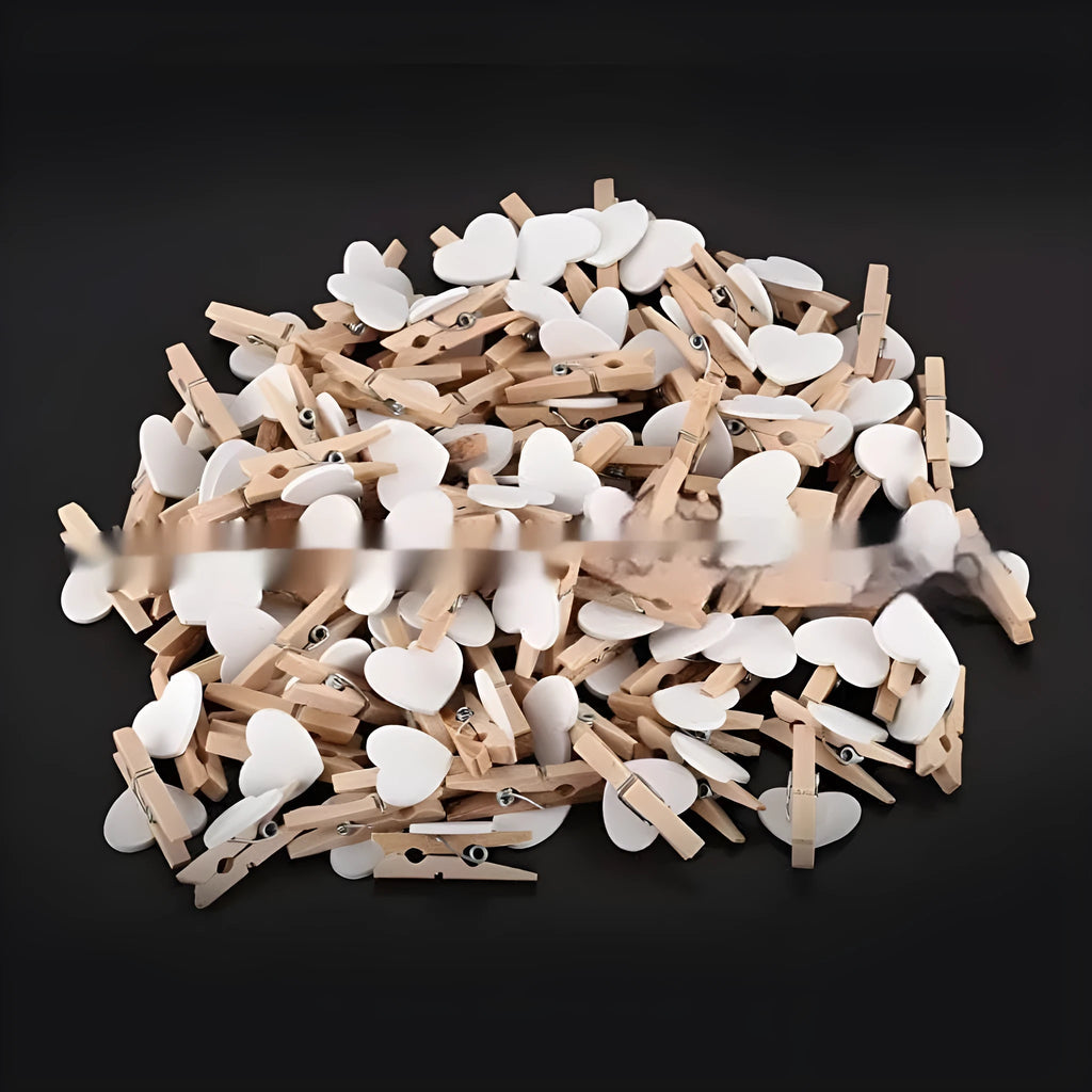 Five small wooden heart-shaped clips in red, pink, white, yellow, and rose colours on a wooden surface.