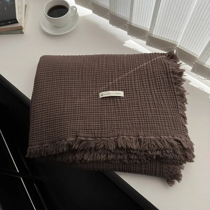 Four-layer gauze cotton blanket with tassel trim in avocado green, laid flat.