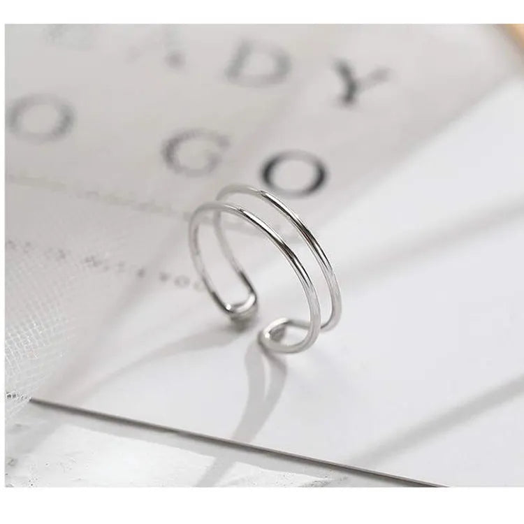 Silver plated geometric cross ring with adjustable opening on a plain background.