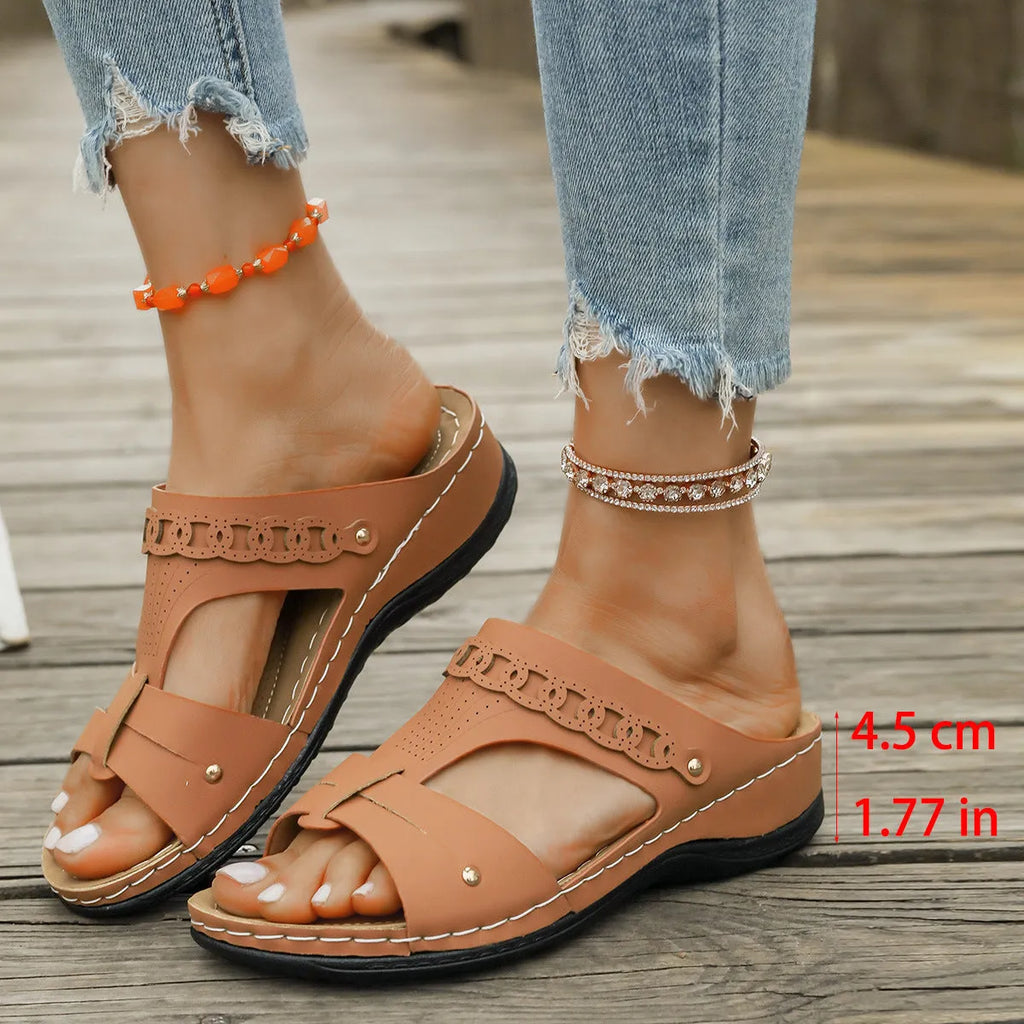 Pair of beige Roman style slippers with a fish mouth toe holder and slope heel on a rubber sole.