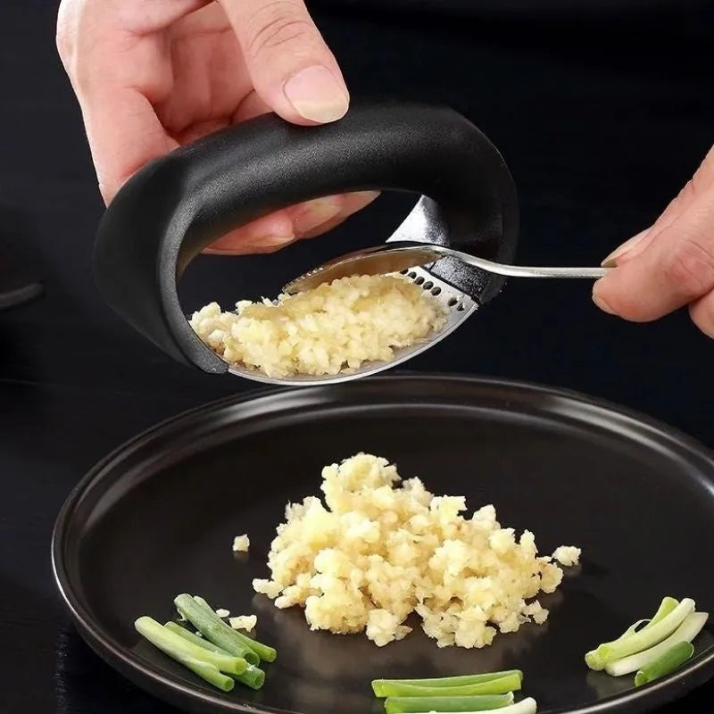 Stainless steel manual garlic press with coloured non-slip handle on a kitchen counter.