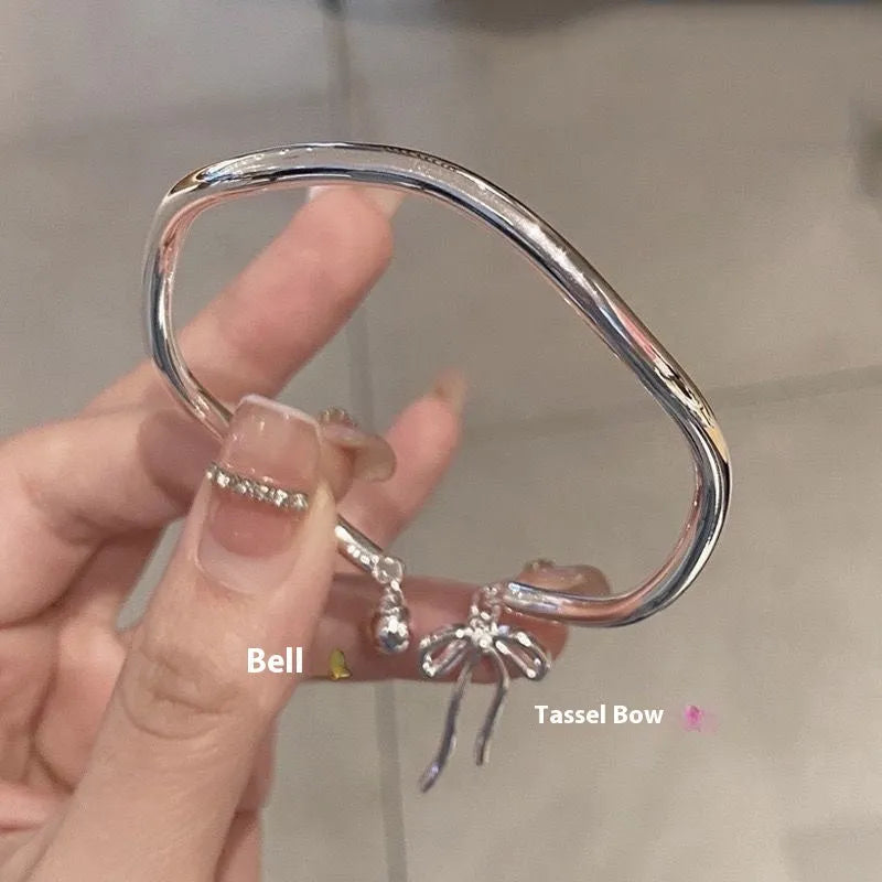 Silver-toned adjustable bracelet with a detailed bow charm on the wrist, showing the opening clasp mechanism.