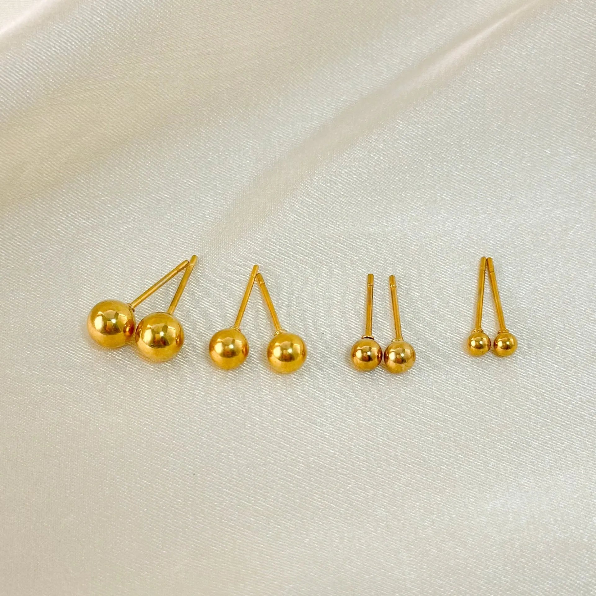Minimalist round ball stud earrings in gold and silver plating on a white background.