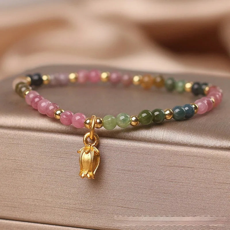 Close-up of a women's beaded anklet with polished tourmaline stones and a detailed metal floral clasp.