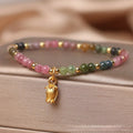 Close-up of a women's beaded anklet with polished tourmaline stones and a detailed metal floral clasp.