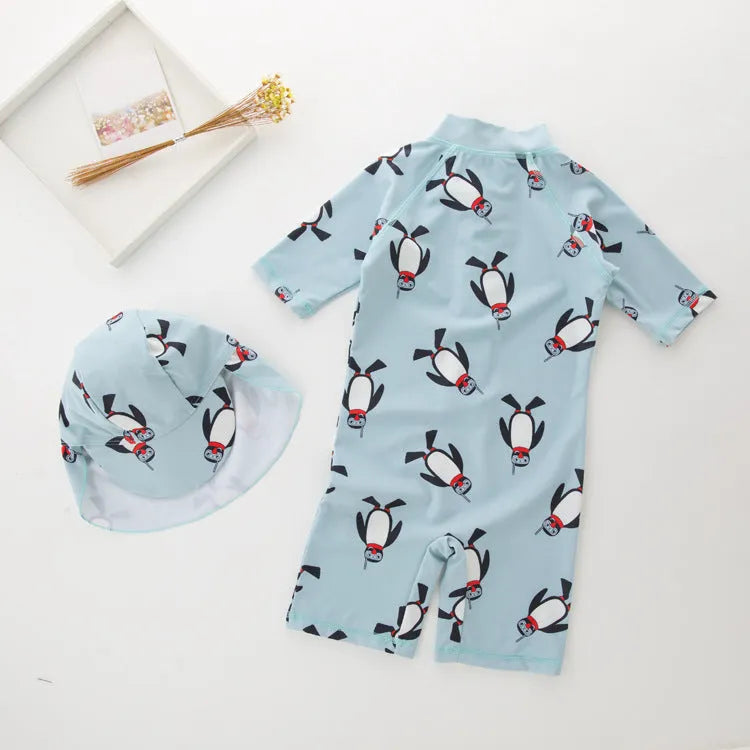 Toddler boy wearing a penguin print long sleeve one-piece swimsuit and matching swimming cap.