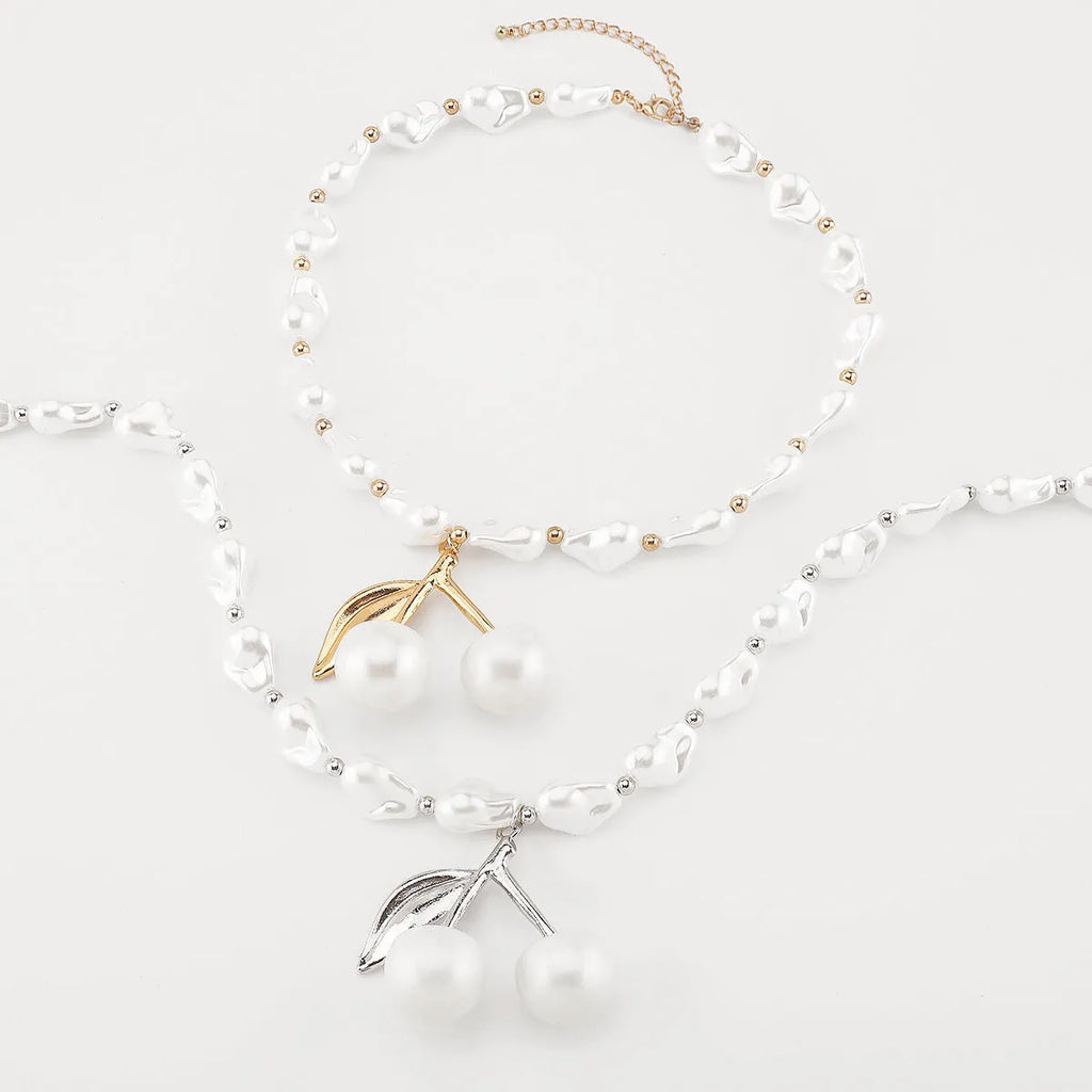 Gold irregular cherry fruit and pearl necklace on adjustable chain against white background.