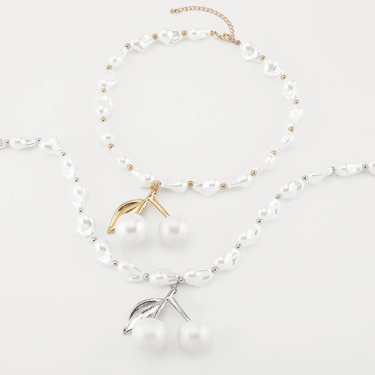 Gold irregular cherry fruit and pearl necklace on adjustable chain against white background.