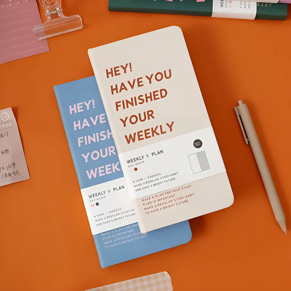 Spiral-bound weekly diary handbook in blue, shown open flat on a table.