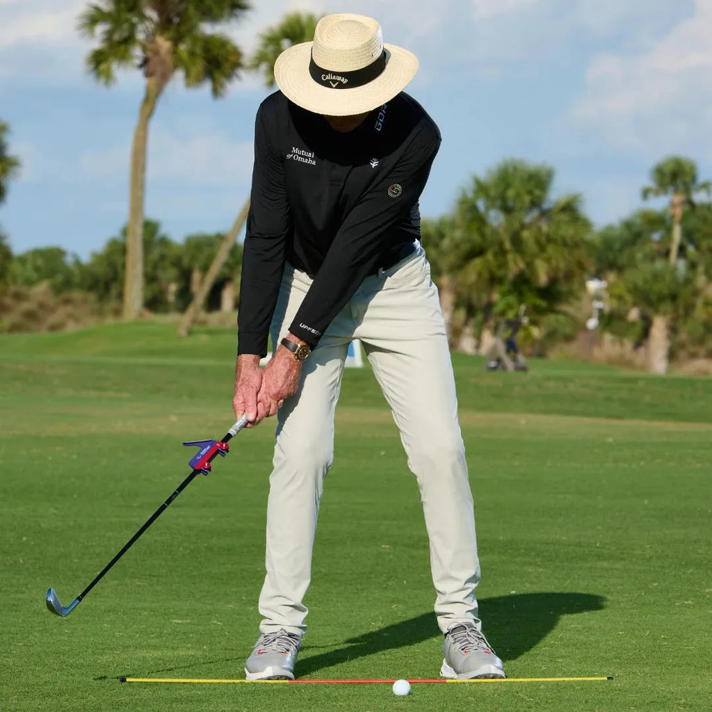 Plastic golf swing plane simulator training aid on a green background.