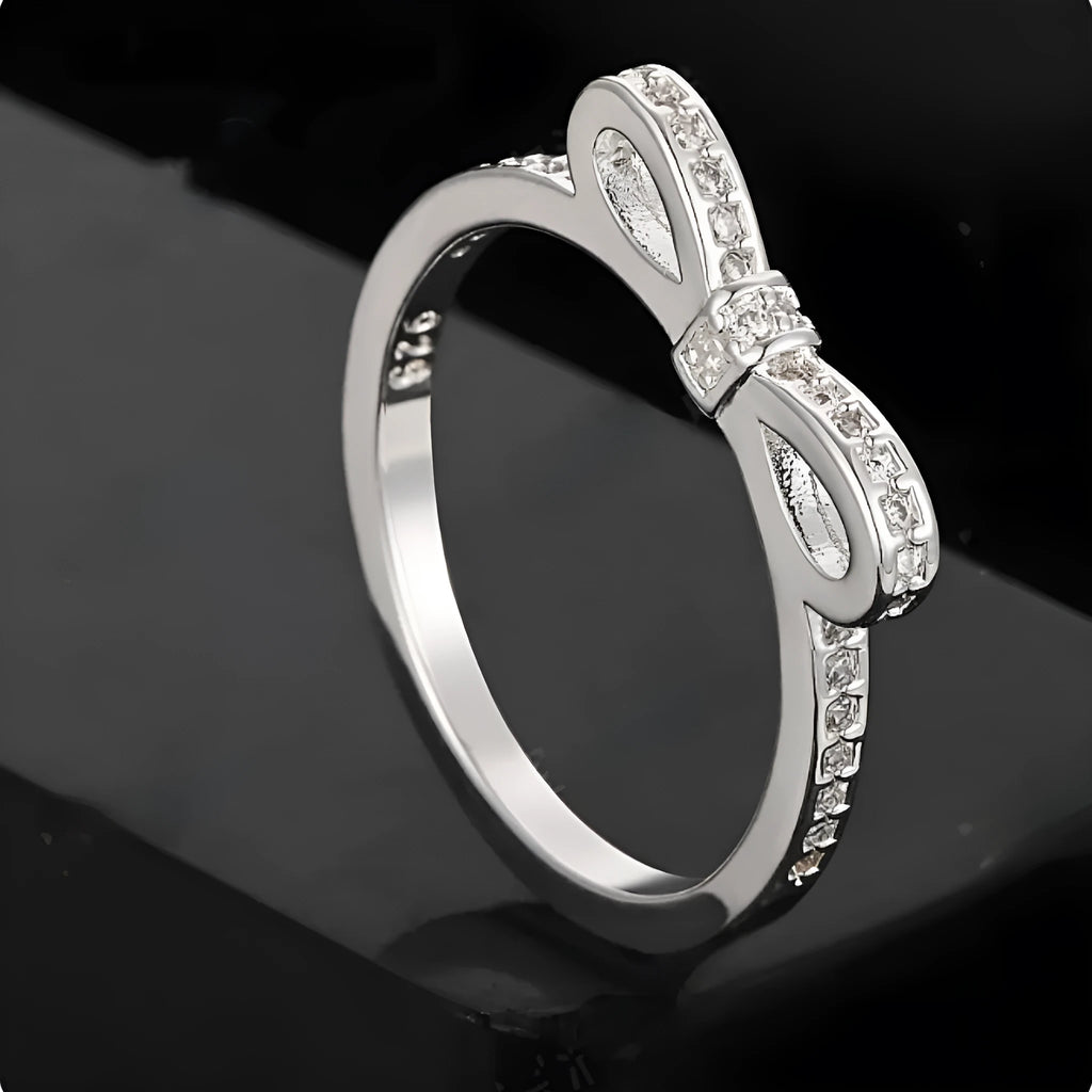 Close-up of a silver bow-shaped ring with sparkling clear zircon crystals on a person's finger.