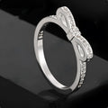 Close-up of a silver bow-shaped ring with sparkling clear zircon crystals on a person's finger.