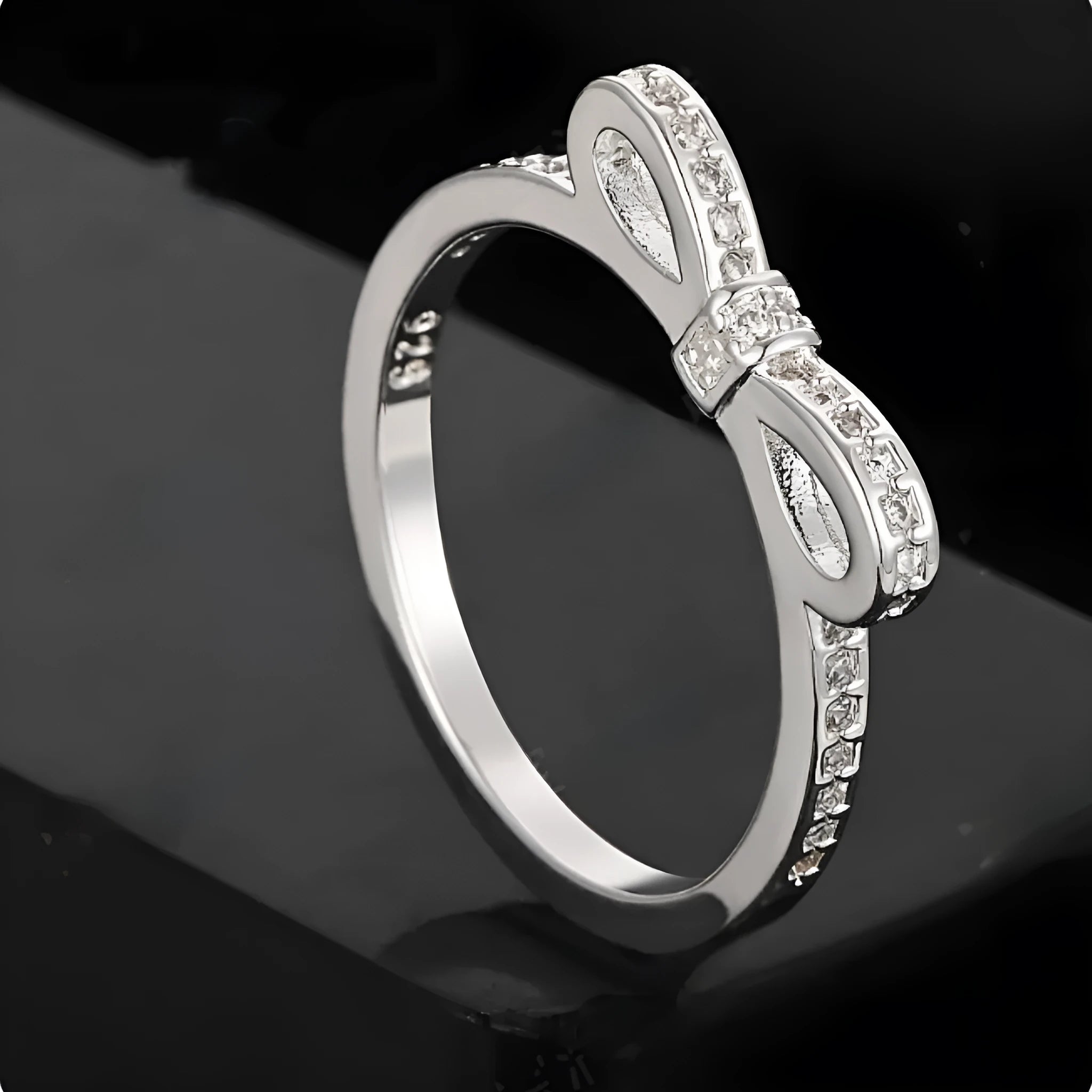 Close-up of a silver bow-shaped ring with sparkling clear zircon crystals on a person's finger.