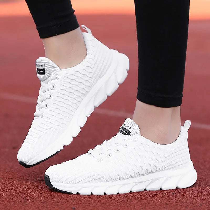Women's running shoes in black, pink, and white colours showing fly weaving upper and rubber outsole.