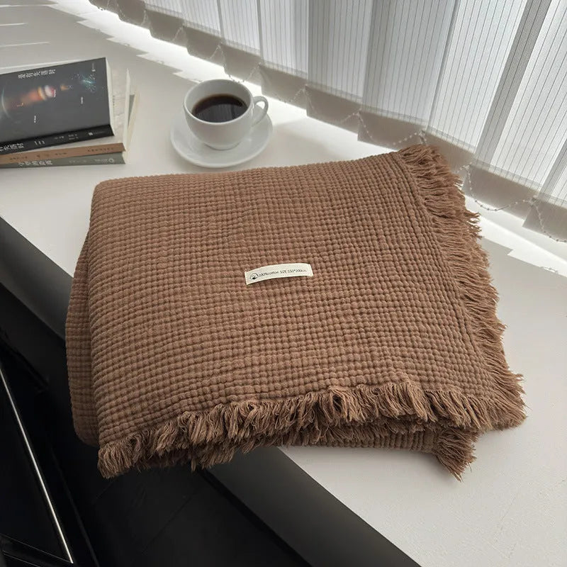 Four-layer gauze cotton blanket with tassel trim in avocado green, laid flat.