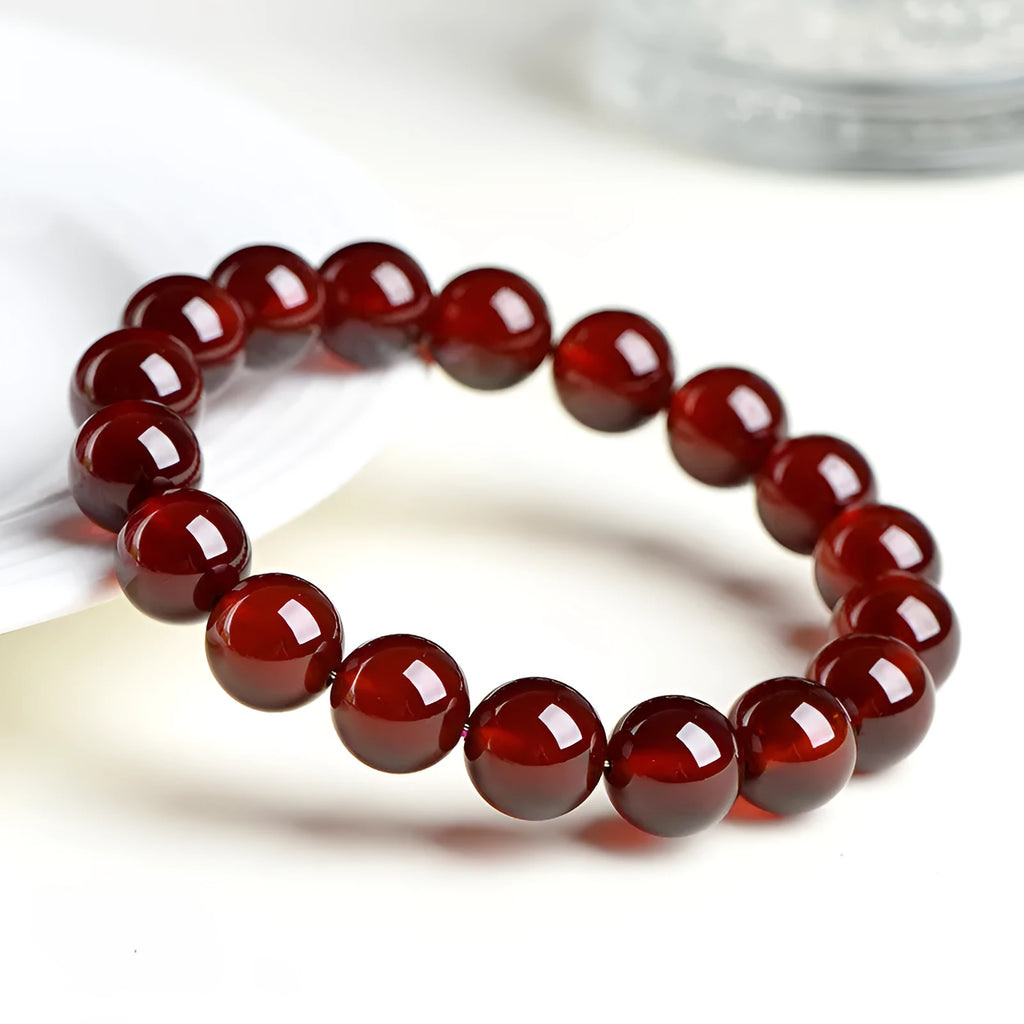 Unisex orange red garnet ball bracelet with crystal beads and a metal Ruyi charm on a wrist.
