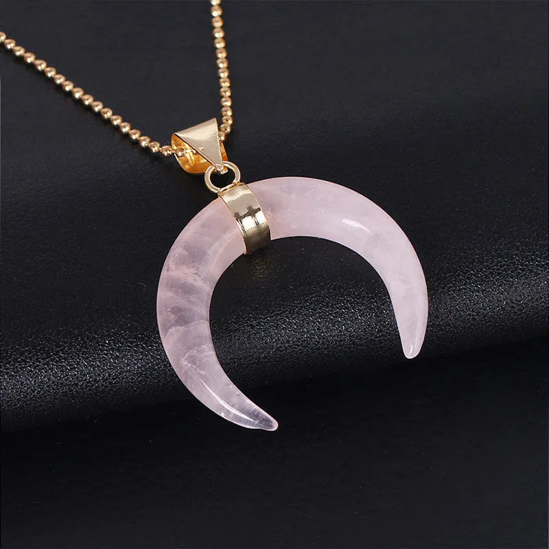 Close-up of a moon-shaped pink natural stone pendant on a metallic chain necklace.