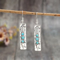 Silver geometric drop earrings with turquoise inlaid accents on a plain background